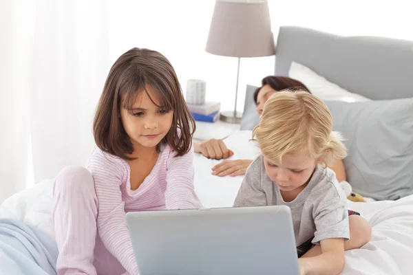 Cute brother and sister on internet while their mother is sleepi — Stock Photo, Image