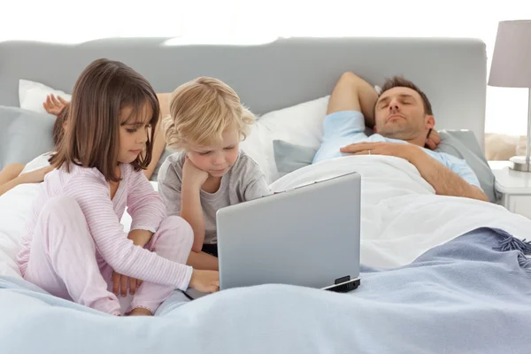 Aufmerksamer Junge mit einem Laptop mit seiner Schwester, während ihre Eltern — Stockfoto