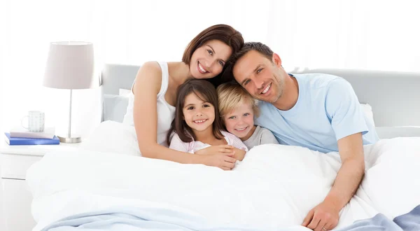 Glückliche Kinder mit ihren Eltern auf dem Bett — Stockfoto
