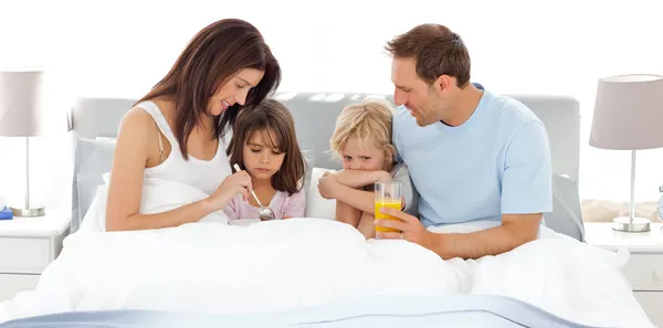 Очаровательные дети завтракают на кровати с родителями — стоковое фото