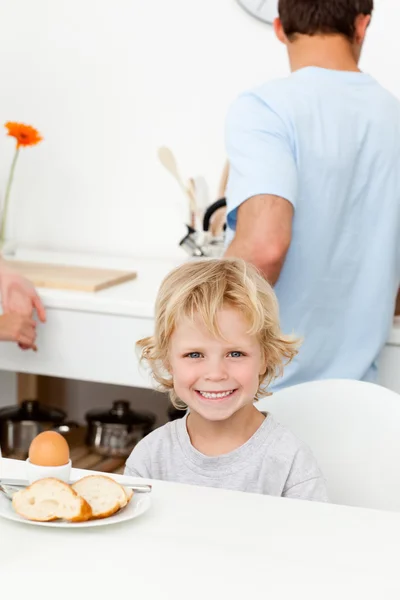 Glücklicher Junge isst gekochtes Ei und Brot in der Küche — Stockfoto