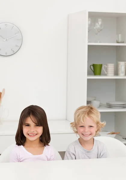 小弟弟和妹妹微笑着坐在一个表中的厨具 — 图库照片