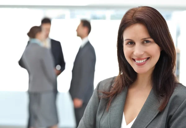 Glad affärskvinna poserar medan hennes team diskuterar — Stockfoto