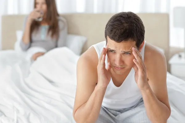 Mann mit Kopfschmerzen sitzt mit Freundin auf dem Bett — Stockfoto