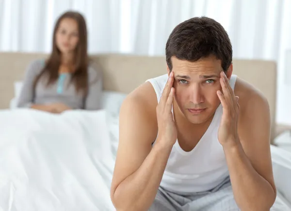 Hombre cansado teniendo un dolor de cabeza sentado en la cama con su novia —  Fotos de Stock