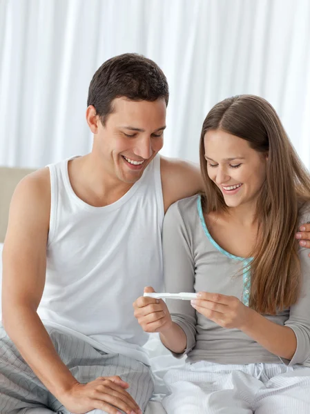 Szczęśliwa para patrząc na test ciążowy na swoim łóżku — Zdjęcie stockowe