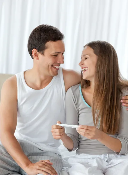 Szczęśliwa para z test ciążowy, siedząc na łóżku — Zdjęcie stockowe