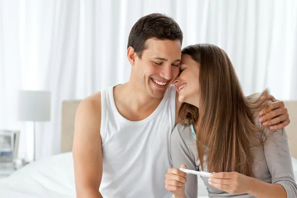 Fröhliches Paar mit Schwangerschaftstest im Schlafzimmer — Stockfoto