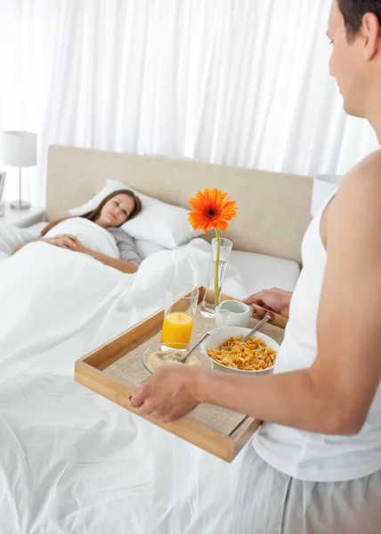 Lovely man bringing the breakfast to his girlfriend lying on the — Stock Photo, Image