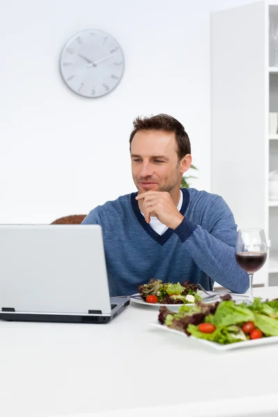 Bonito homem olhando para seu laptop enquanto almoça — Fotografia de Stock