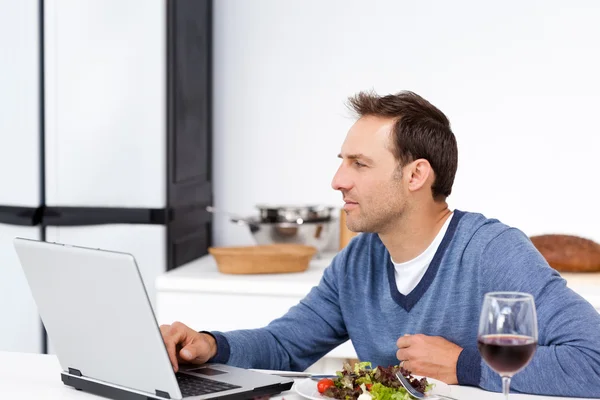 Hombre concentrado mirando su portátil mientras come una ensalada — Foto de Stock