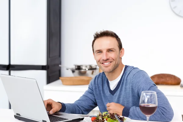Glücklicher Mann, der beim Salatessen auf seinen Laptop schaut — Stockfoto