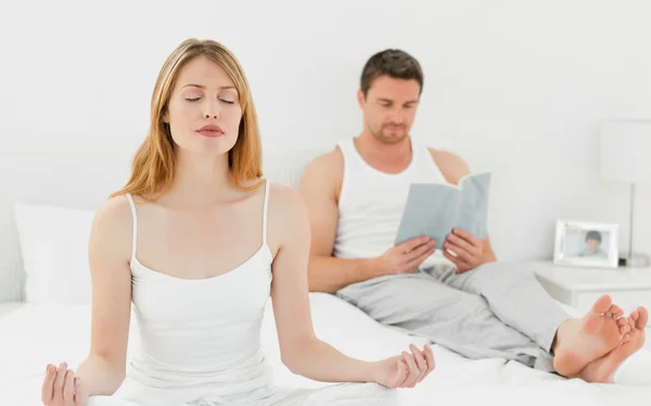 Femme pratique le yoga pendant que son mari lit — Photo