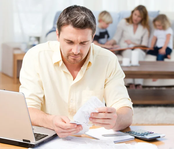 Hombre calculando sus facturas mientras su familia está en el sofá —  Fotos de Stock