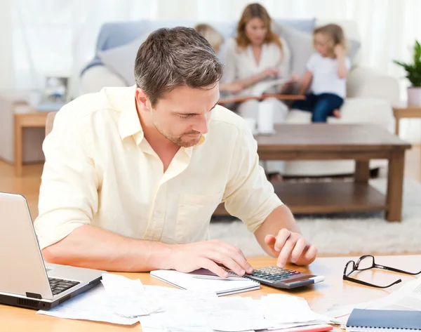 Mann berechnet seine Rechnungen, während seine Familie auf dem Sofa sitzt — Stockfoto