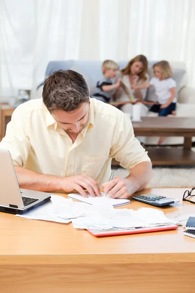 Hombre calculando sus facturas mientras su familia está en el sofá — Foto de Stock