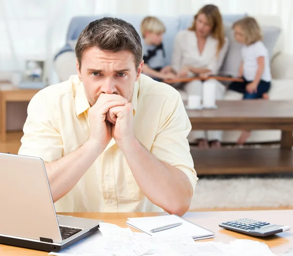 Homem calculando suas contas enquanto sua família está no sofá — Fotografia de Stock