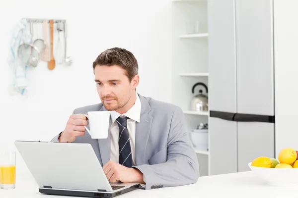Affärsman dricka medan han tittar på sin laptop — Stockfoto