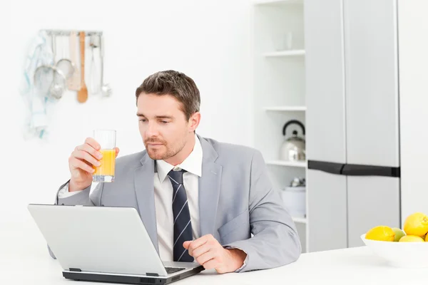 Biznesmen picia, podczas gdy on patrzy na jego laptopie — Zdjęcie stockowe