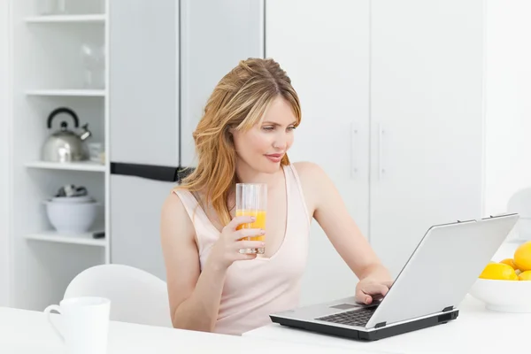 Жінка п'є, поки вона дивиться на свій ноутбук — стокове фото