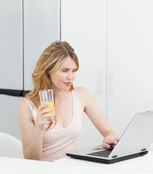 Frau trinkt, während sie auf ihren Laptop schaut — Stockfoto