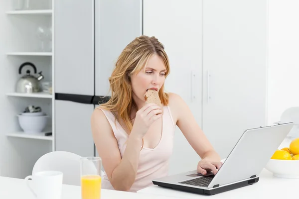 Mulher bebendo enquanto ela está olhando para seu laptop — Fotografia de Stock