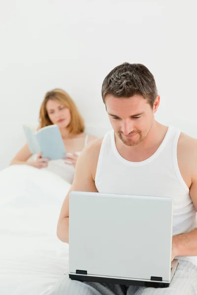 Člověk je na jeho laptopu, zatímco jeho žena čte knihu — Stock fotografie