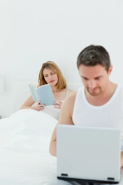 L'homme est sur son ordinateur portable pendant que sa femme lit un livre — Photo