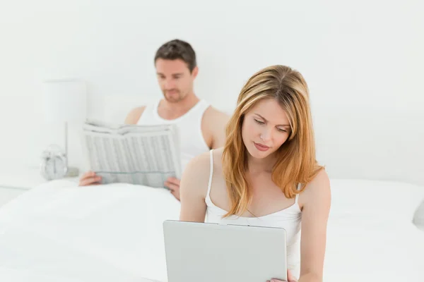 彼女の夫は新聞を読んでいる間女性は彼女のラップトップ — ストック写真