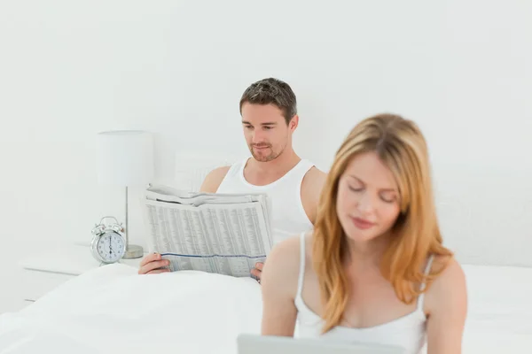 Женщина сидит за ноутбуком, пока ее муж читает газету. — стоковое фото