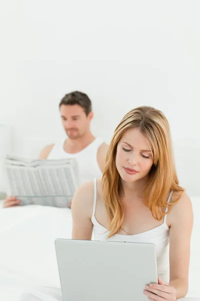 Woman is on her laptop while her husband is reading newspaper — Stock Photo, Image