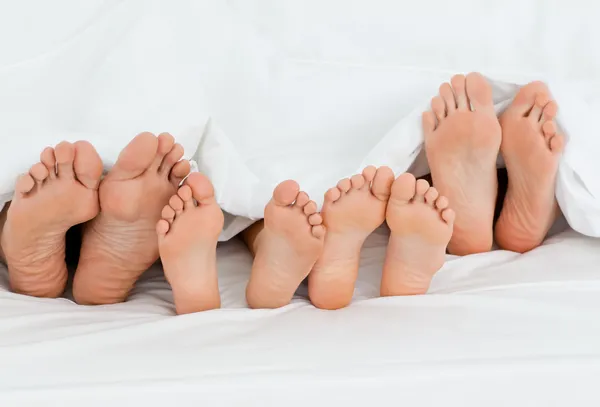 Rodina na posteli doma s nohama, ukazuje — Stock fotografie