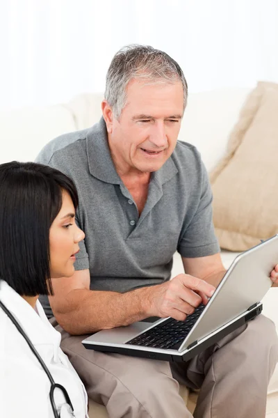 Volwassen man met zijn verpleegster kijken naar de laptop thuis — Stockfoto