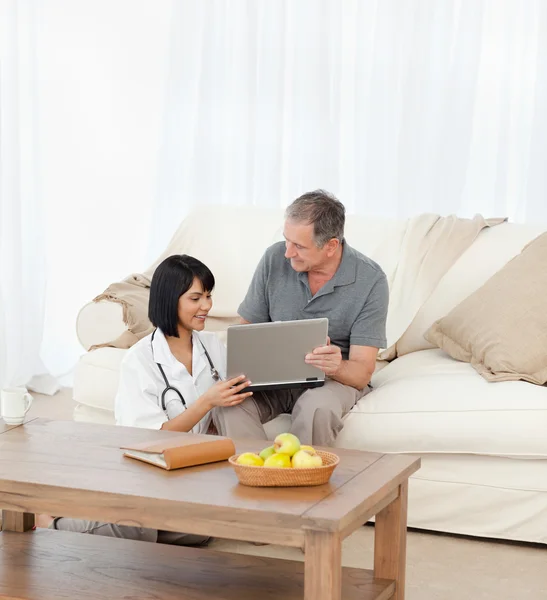 Mature man with his nurse looking at the laptop at home — Stock Photo, Image