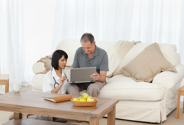 Homem maduro com sua enfermeira olhando para o laptop em casa — Fotografia de Stock