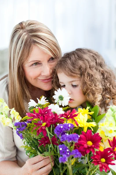 Malá holčička vonící květy, zatímco její babička je smilling — Stock fotografie