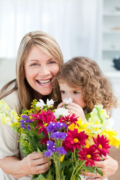 Klein meisje ruikende bloemen, terwijl haar grootmoeder smilling is — Stockfoto