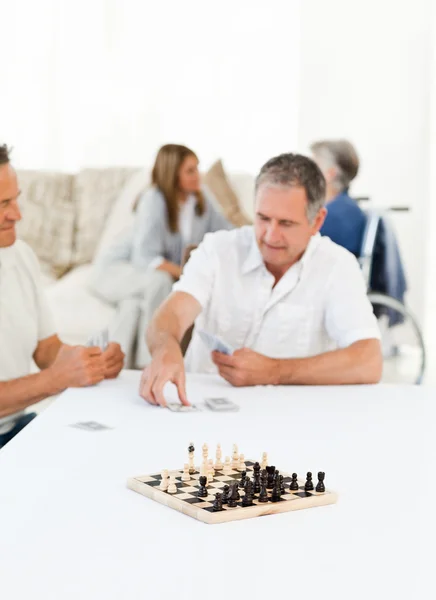 Hombres jugando a las cartas mientras sus esposas están hablando —  Fotos de Stock