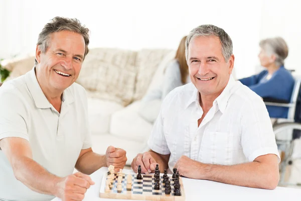 Чоловіки грають в шахи, поки їх дружини говорять — стокове фото