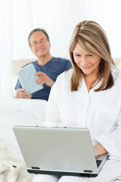 Femme regardant son ordinateur portable pendant que son mari lit — Photo