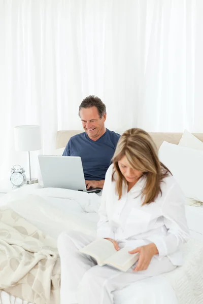 Старший дивиться на свій ноутбук, поки її дружина читає — стокове фото