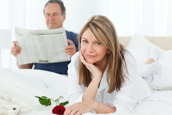 Glückliche Frau mit ihrer Rose, während ihr Mann eine Zeitung liest — Stockfoto