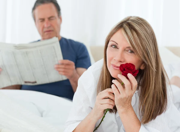 Mulher feliz cheirando sua rosa enquanto seu marido está lendo um novo — Fotografia de Stock