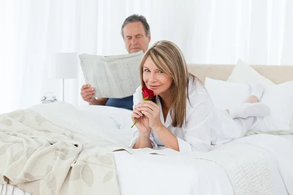 Donna felice con la sua rosa mentre suo marito sta leggendo una newspap — Foto Stock