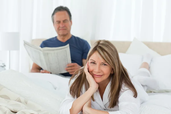 Sorridente donna guardando la fotocamera mentre suo marito è readin — Foto Stock