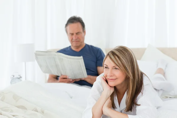 Donna sorridente mentre suo marito sta leggendo — Foto Stock