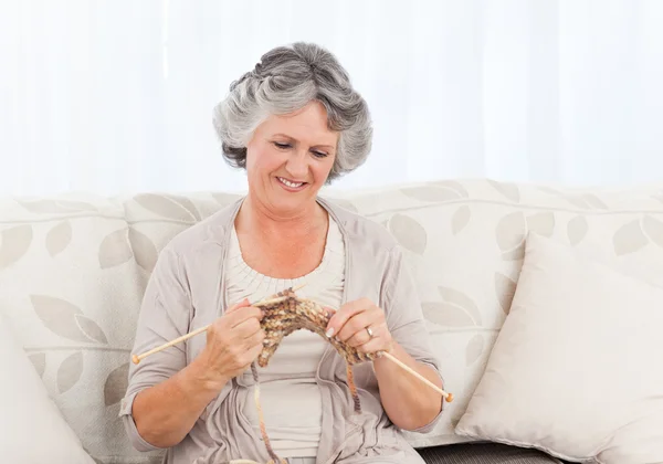 Starší žena pletení na jejím gauči — Stock fotografie