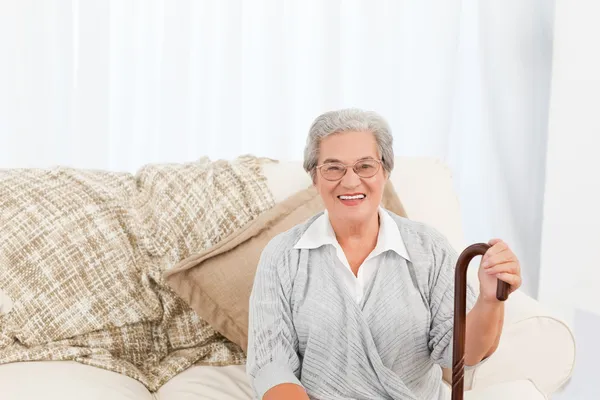 Reife Frau sitzt mit ihrem Gehstock auf dem Sofa — Stockfoto