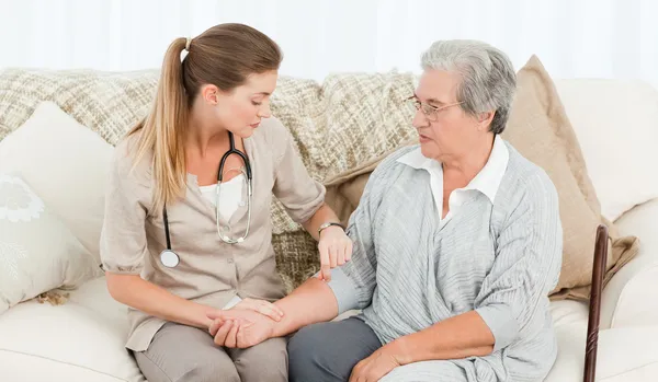 Beautiful nurse taking the pulse of her patient at home — Stock Photo, Image