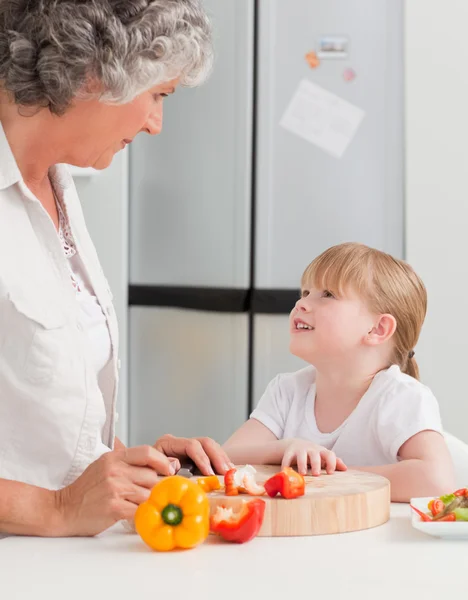 Little girl looking at her grandmother who is cooking — Stock Photo, Image
